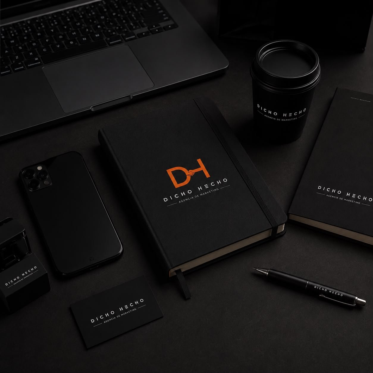 Detalle de mesa de trabajo de Dicho y Hecho con portátil, libreta de marca y móvil